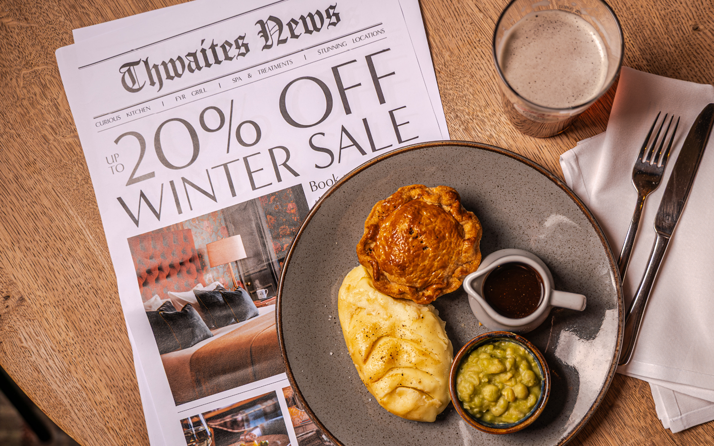 "up to 20% off this winter" newspaper with pie and a pint flat lay at a pub table